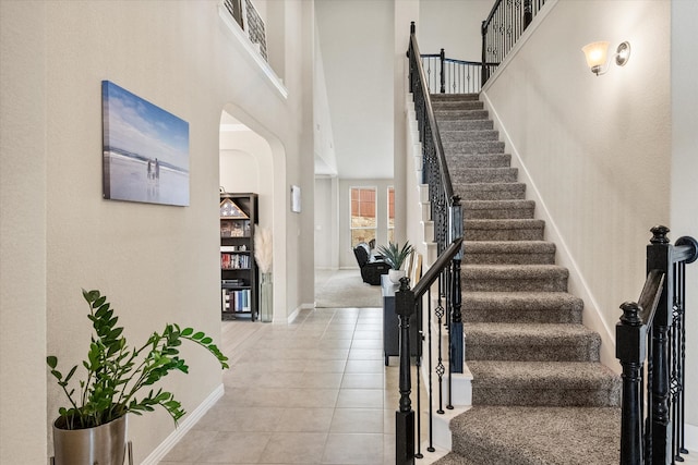 stairway with baseboards, a high ceiling, tile patterned floors, and arched walkways
