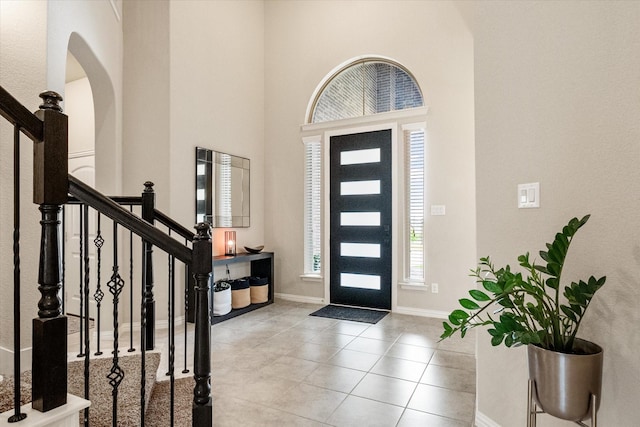entrance foyer with a towering ceiling, baseboards, stairway, tile patterned floors, and arched walkways