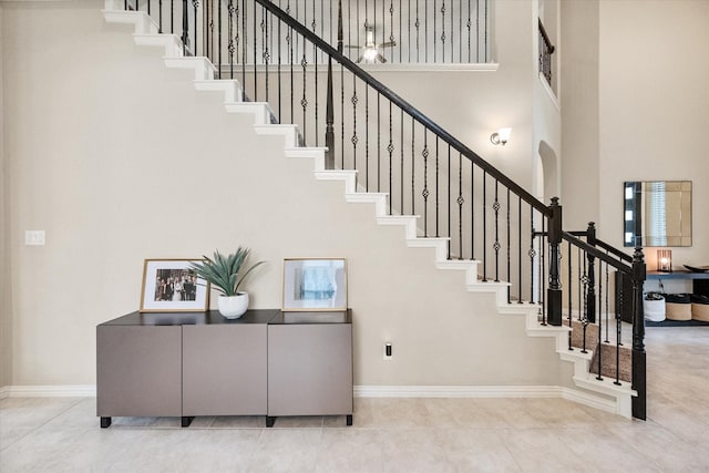 staircase with baseboards, a high ceiling, and tile patterned floors