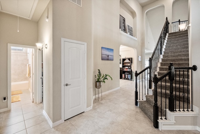 entryway featuring arched walkways, a high ceiling, baseboards, and tile patterned flooring