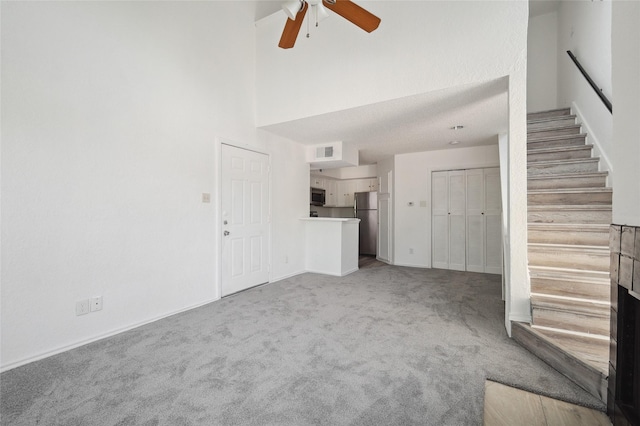 unfurnished living room with visible vents, a towering ceiling, ceiling fan, stairway, and carpet