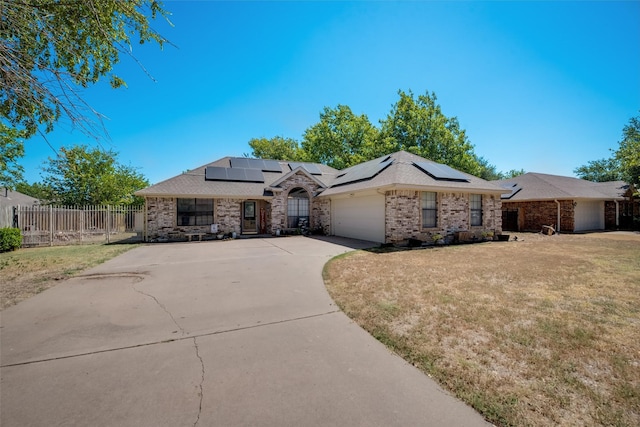 ranch-style house with roof mounted solar panels, an attached garage, concrete driveway, and brick siding