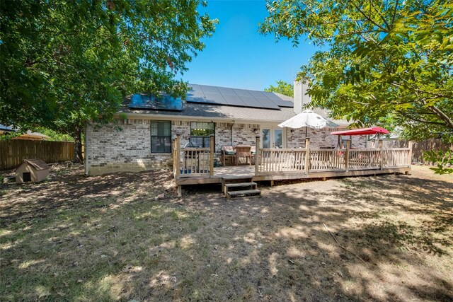 back of property with solar panels, a chimney, a wooden deck, brick siding, and fence