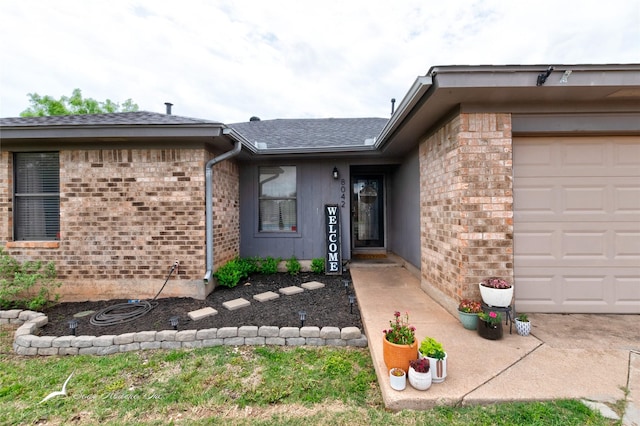 entrance to property with brick siding, a garage, and a shingled roof