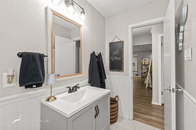 bathroom with vanity, wainscoting, and a decorative wall