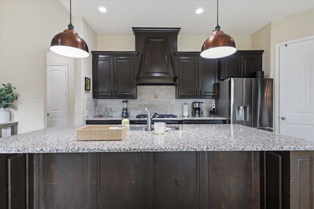 kitchen with light stone counters, stainless steel fridge, premium range hood, a large island, and backsplash