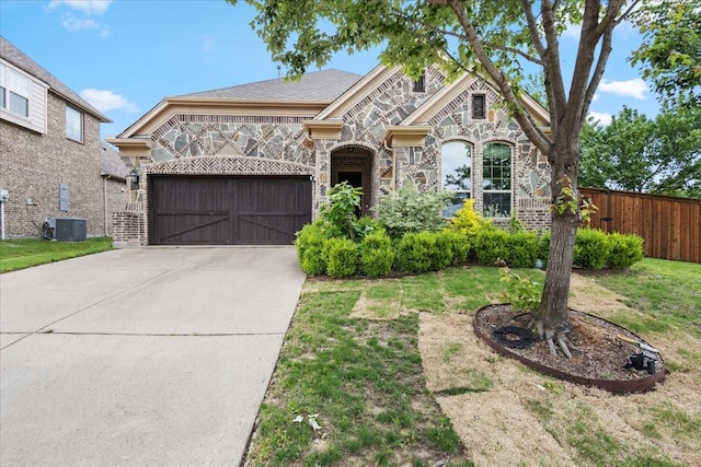 french provincial home featuring central AC, fence, stone siding, an attached garage, and driveway