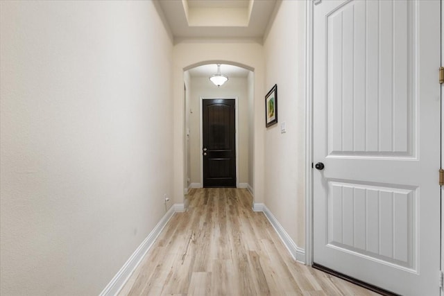doorway with arched walkways, baseboards, and light wood-type flooring