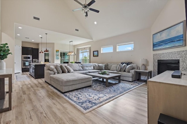 living area featuring visible vents, ceiling fan, high vaulted ceiling, light wood-type flooring, and a tiled fireplace