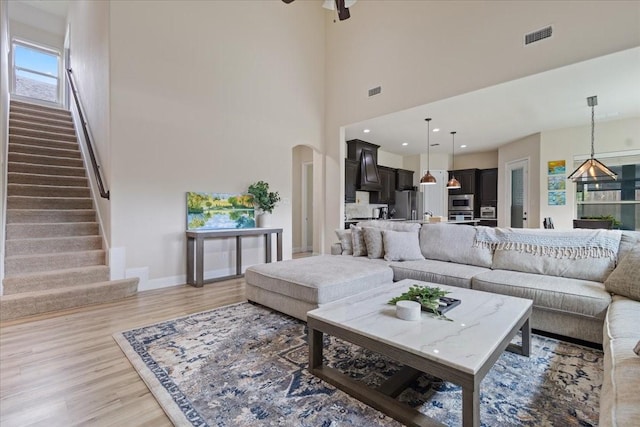 living room featuring a ceiling fan, stairs, baseboards, arched walkways, and light wood-style flooring