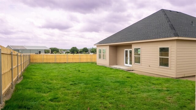 rear view of house featuring a fenced backyard, a shingled roof, and a yard