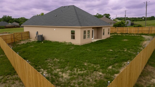 rear view of property with a lawn, a fenced backyard, central air condition unit, and a shingled roof