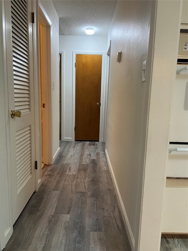 corridor featuring a textured ceiling, dark wood-style floors, and baseboards