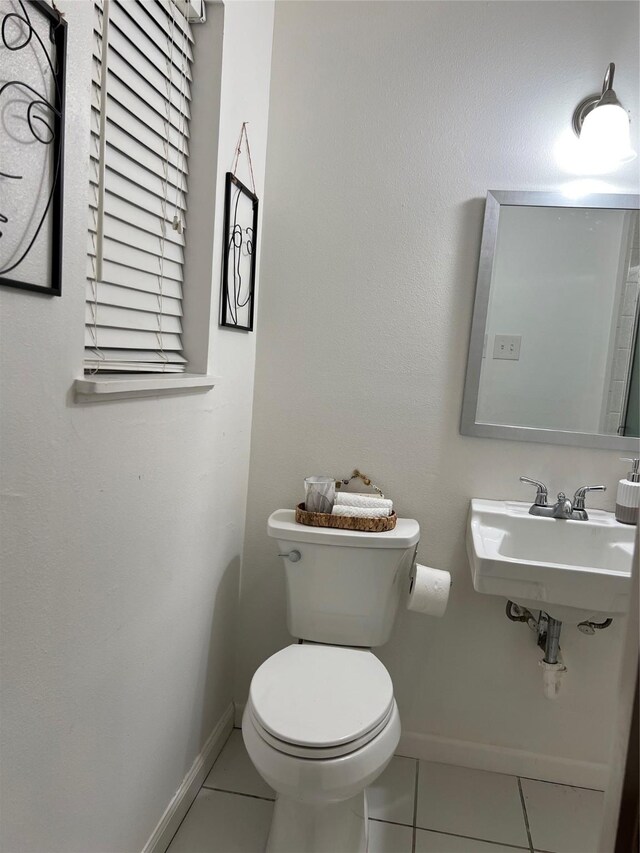 bathroom featuring toilet, baseboards, a sink, and tile patterned flooring