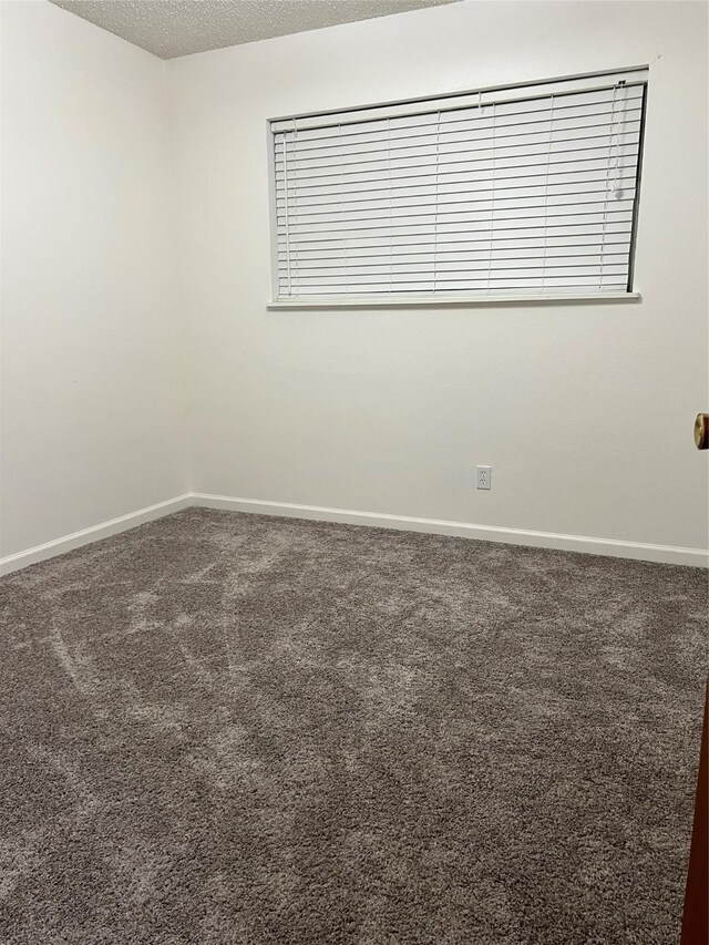 empty room featuring a textured ceiling, baseboards, and carpet