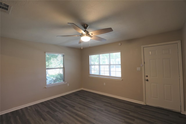 empty room featuring dark wood-style flooring, baseboards, visible vents, and ceiling fan
