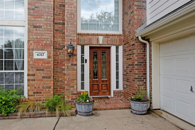entrance to property featuring a garage and brick siding