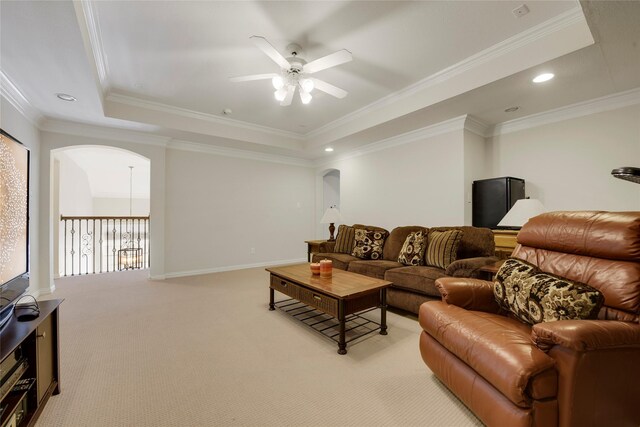 living area featuring a ceiling fan, ornamental molding, light carpet, a raised ceiling, and arched walkways