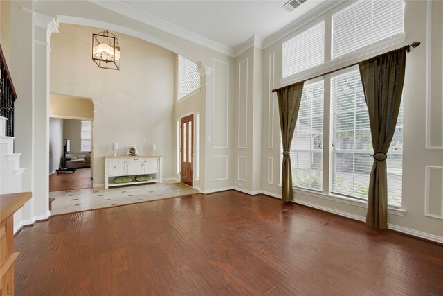 unfurnished living room with visible vents, ornamental molding, wood finished floors, a high ceiling, and arched walkways