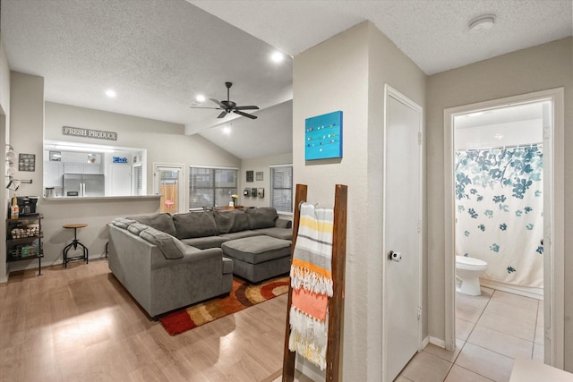 living area featuring light wood-style floors, a textured ceiling, ceiling fan, and vaulted ceiling