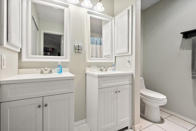 bathroom with a sink, tile patterned flooring, toilet, baseboards, and two vanities