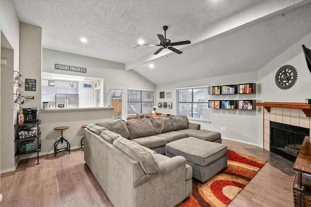 living area with a ceiling fan, a textured ceiling, a fireplace, vaulted ceiling, and wood finished floors