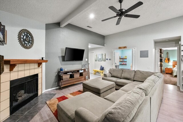 living room with a textured ceiling, vaulted ceiling with beams, wood finished floors, a tile fireplace, and visible vents