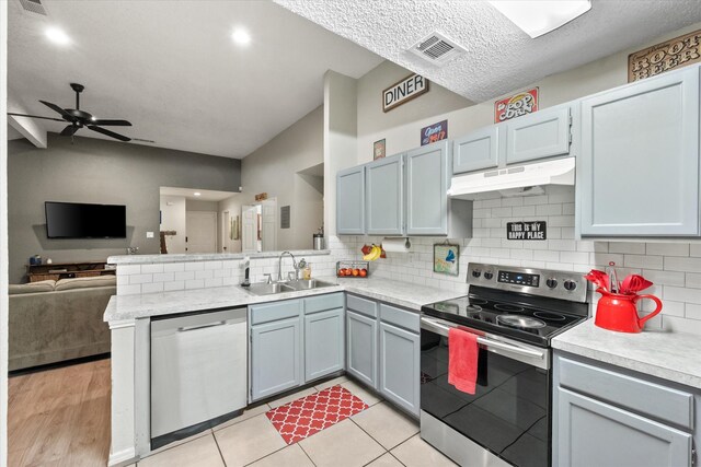 kitchen with a peninsula, light countertops, under cabinet range hood, a sink, and stainless steel appliances
