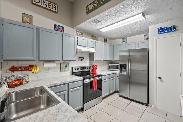 kitchen with a sink, light countertops, stainless steel appliances, tasteful backsplash, and under cabinet range hood
