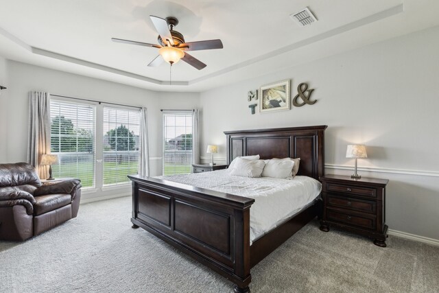 bedroom featuring a ceiling fan, a tray ceiling, visible vents, and light carpet