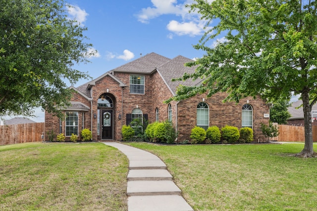 view of front of home with brick siding, a front lawn, and fence