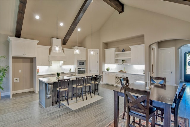 kitchen featuring open shelves, beamed ceiling, custom range hood, arched walkways, and stainless steel appliances