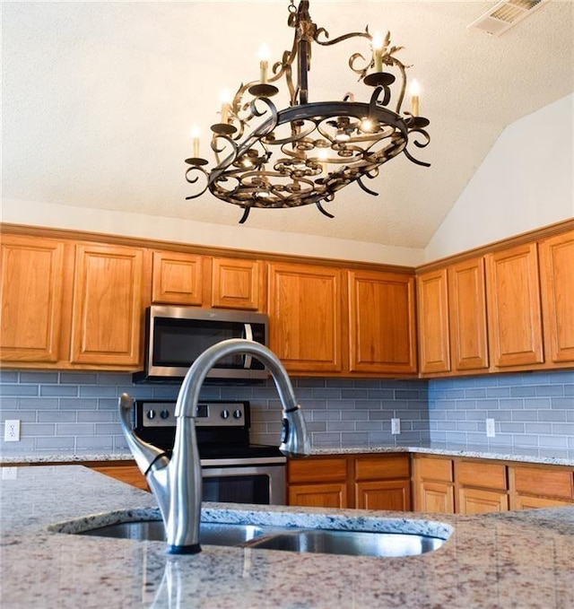 10408 Ambergate Ln, Frisco, TX 75035 - kitchen with visible vents, lofted ceiling, a chandelier, brown cabinets, and appliances with stainless steel finishes