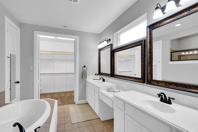 bathroom featuring visible vents, double vanity, a spacious closet, a sink, and tiled bath