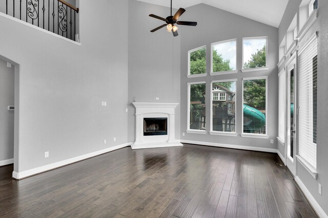 unfurnished living room with ceiling fan, dark wood finished floors, baseboards, high vaulted ceiling, and a fireplace with raised hearth
