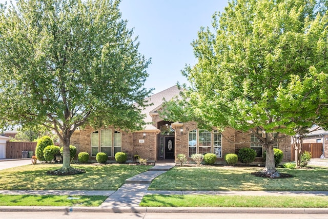 view of property hidden behind natural elements featuring fence, a front yard, and brick siding