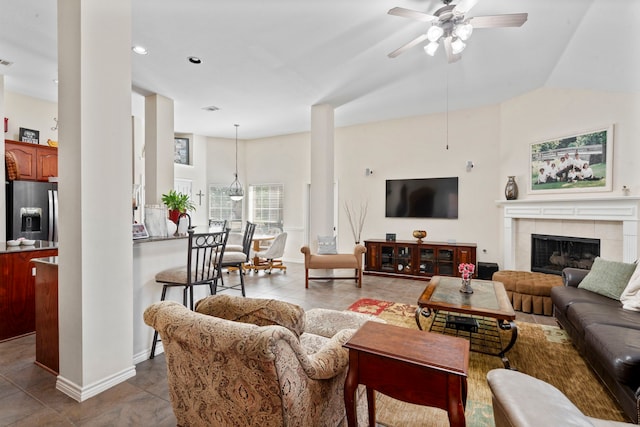 living area featuring a tiled fireplace, a ceiling fan, baseboards, and vaulted ceiling