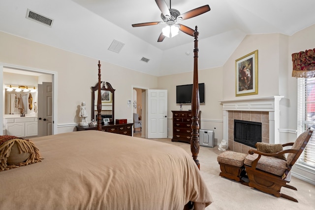 carpeted bedroom with visible vents, a tiled fireplace, ensuite bathroom, and vaulted ceiling
