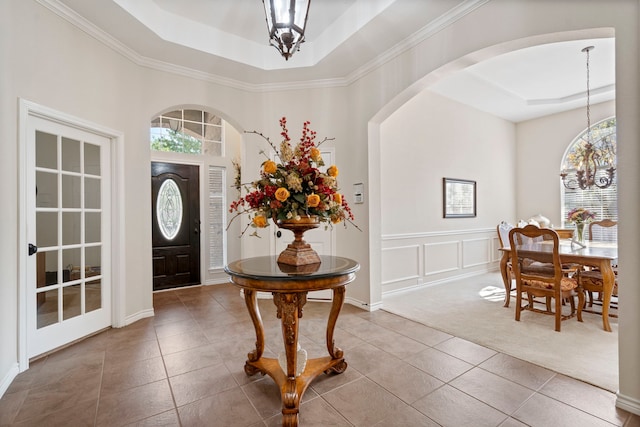 entryway featuring crown molding, a notable chandelier, arched walkways, tile patterned floors, and a tray ceiling