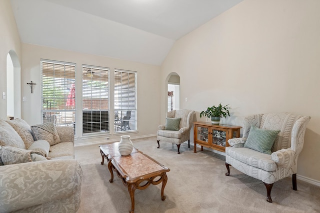 living room featuring baseboards, arched walkways, vaulted ceiling, and light carpet