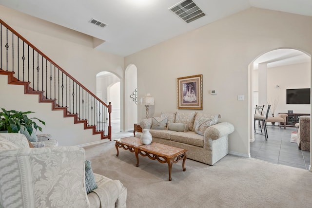 carpeted living area with arched walkways, baseboards, visible vents, and stairway