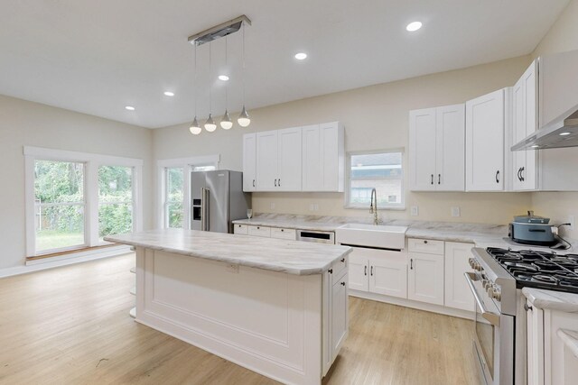 kitchen with premium appliances, a sink, light wood finished floors, and a center island