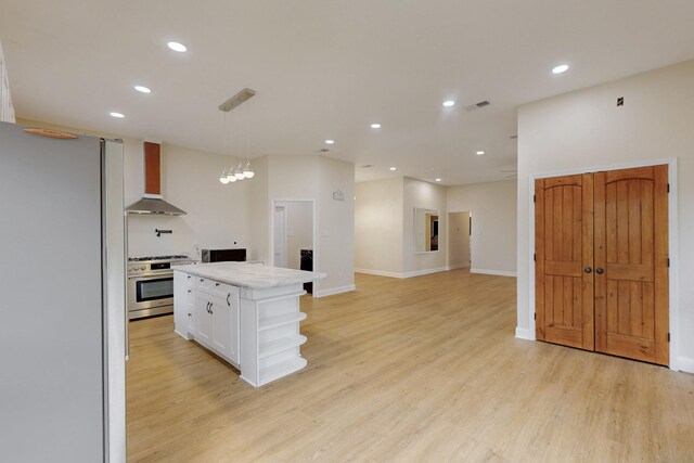 kitchen featuring light wood-type flooring, stainless steel gas stove, white cabinets, freestanding refrigerator, and wall chimney exhaust hood