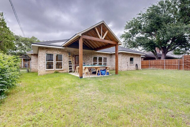 rear view of house featuring brick siding, a patio area, fence, and a yard