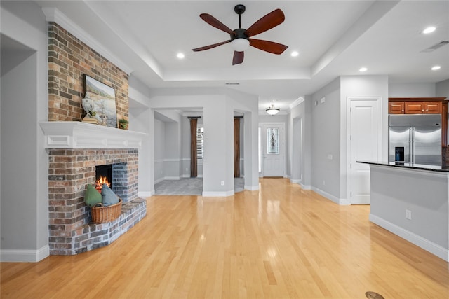 unfurnished living room featuring visible vents, a brick fireplace, ceiling fan, a raised ceiling, and light wood-style flooring
