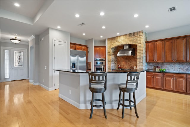 kitchen with visible vents, wall chimney exhaust hood, appliances with stainless steel finishes, and a center island with sink