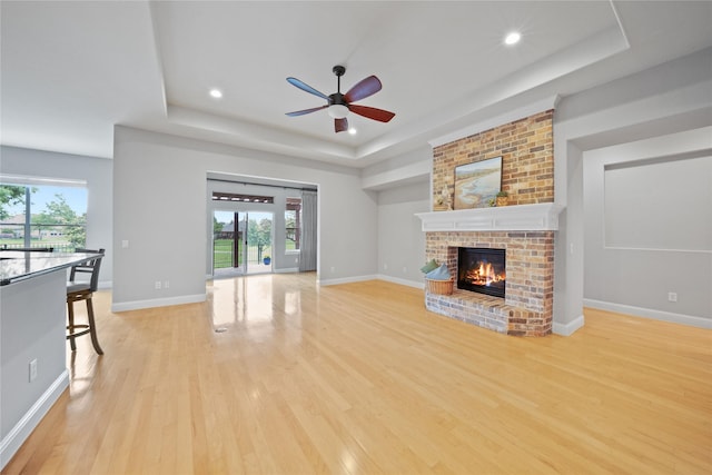 unfurnished living room featuring a ceiling fan, a wealth of natural light, a raised ceiling, and light wood-type flooring