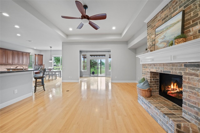 living room featuring a brick fireplace, light wood-style floors, baseboards, ceiling fan, and recessed lighting