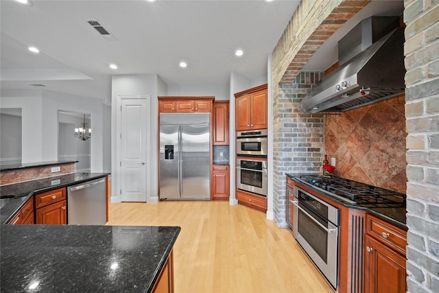 kitchen featuring visible vents, wall chimney exhaust hood, a notable chandelier, stainless steel appliances, and light wood-style flooring