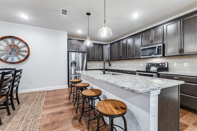 kitchen with a kitchen breakfast bar, visible vents, a center island with sink, a sink, and stainless steel appliances